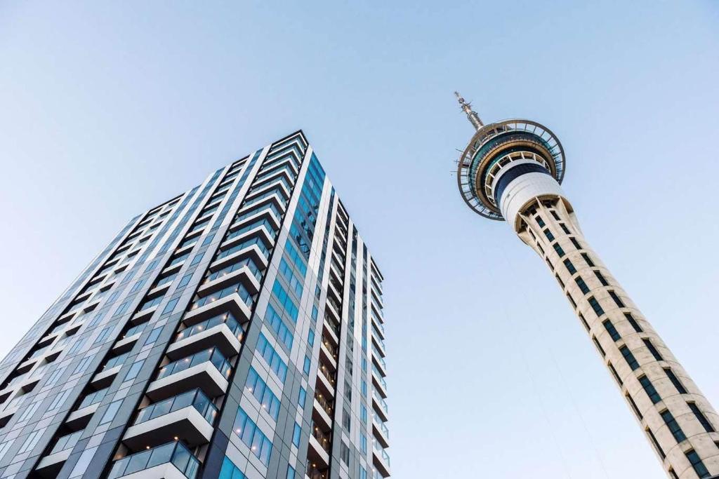 Looking up at the Sky Tower and a glass apartment building in central Auckland, against a clear sky